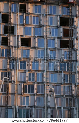 View of the grey facade of a high building in construction. Many reflective windows. Patterns with rectangles and lines. Purple color beacause of the reflection of the sky. Urban futuristic design. 