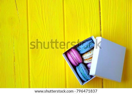 French macaroon sweets, different tastes & colors. Box of macarons on yellow timber wooden texture table background. Birthday valentine spring present. Copy text space, flat lay, top front view.