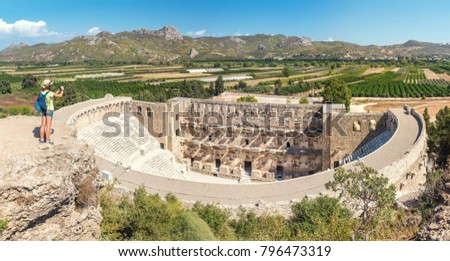 Young tourist woman take a photo of the antique amphitheater Aspendos in Turkey