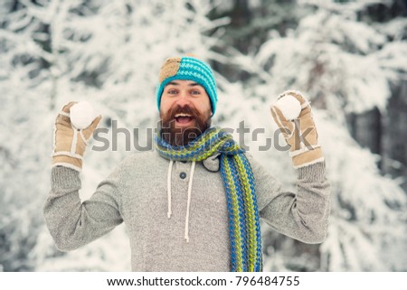 Bearded man smile with snowballs in snowy forest. Hipster in thermal jacket, hat, scarf, beard warm in winter. Skincare, beard care in winter. Temperature, freezing, cold snap. Snow fight, sport, rest
