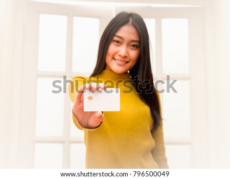 Cute girl standing and show a white card with microship on right hand. (Selective focus white card)