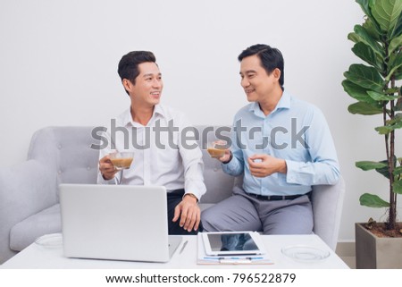Two confident young businesspeople using a laptop discuss information while sitting on a sofa in a modern office