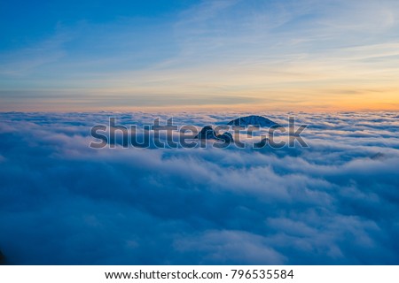 Background photo of low clouds in a mountain valley, vibrant blue and orange sky. Sunrise or sunset view of mountains and peaks peaking through clouds. Winter alpine like landscape of high Tatras. Royalty-Free Stock Photo #796535584