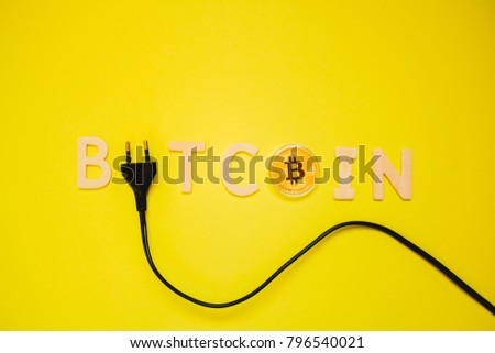 Word bitcoin made from wooden letters, a bitcoin coin and an AC power plug on a bright yellow pastel background. Power consumption done by cryptocurrency mining concept