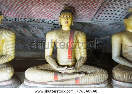Group of sitting Buddha statues in cave buddhist temple with bright painted murals on walls and ceiling in Dambulla golden temple on Sri Lanka island