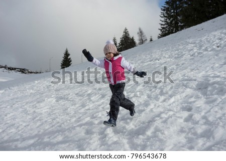 A  little girl is playng running on snowy slope. Negative space, copy space.