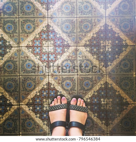 Selfie of feet with shoes on art pattern tiles floor, top view