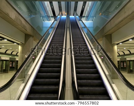 Escalator at an airport with no people. Two escalators in symmetry going up and down inside an airport going from one floor to the other. Modern and sleek interior an airport. Steal, metal, shinny.