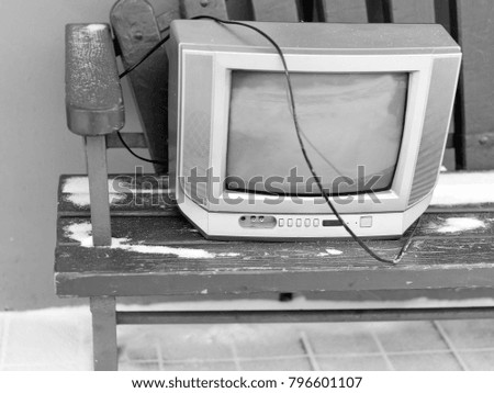 Old tv set on the bench, seems abanoned. In black and white