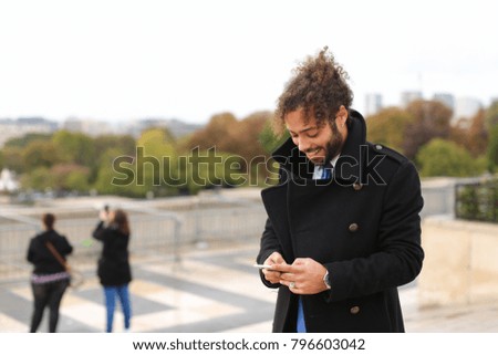 Handsome tourist using smartphone and enjoying France travel in slow motion.  Attractive guy dressed in black coat with earring and curly hair calling girlfriend. Concept of European trip an