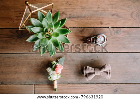 Wedding rings with succulent in glassed box, watch and boutonniere on wooden background. Flat lay. Top view