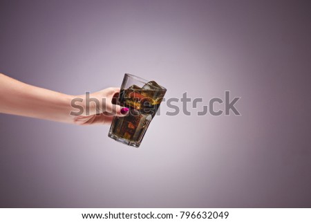 Drink cola in glass with hand on lilac background.