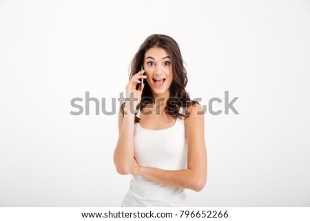 Portrait of a surprised girl dressed in tank-top talking on mobile phone isolated over white background