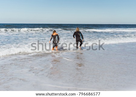 man and woman go to the ocean with surf boards. man and girl go surfing, Portugal, Nazare. Surfing in a wet suit.