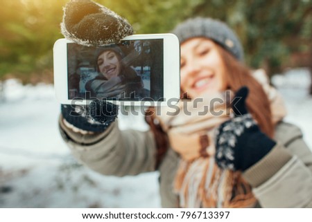 Young woman takes selfie in winter forest with her smartphone