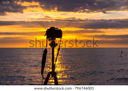 Silhouette of a tripod with a camera on a background of a sea landscape with a bright orange evening sky. Beautiful colorful sunset in Adler, Sochi, Russia.