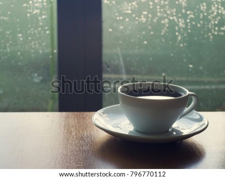 White cup of coffee on wooden table near a window with water drow bokeh in a cross process picture style