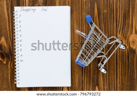 shopping list with empty shopping cart on wooden background