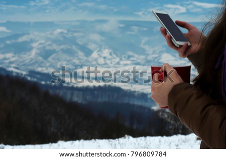 A girl with a red mug in the snow-capped mountains, holds and looks in the phone