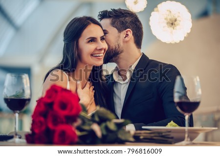 Beautiful loving couple is spending time together in modern restaurant. Attractive young woman in dress and handsome man in suit are having romantic dinner. Celebrating Saint Valentine's Day. Royalty-Free Stock Photo #796816009