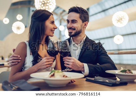 Beautiful loving couple is spending time together in modern restaurant. Attractive young woman in dress and handsome man in suit are having romantic dinner. Celebrating Saint Valentine's Day. Royalty-Free Stock Photo #796816114