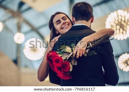 Beautiful loving couple is spending time together in modern restaurant. Attractive young woman in dress and handsome man in suit are having romantic dinner. Celebrating Saint Valentine's Day. Royalty-Free Stock Photo #796816117