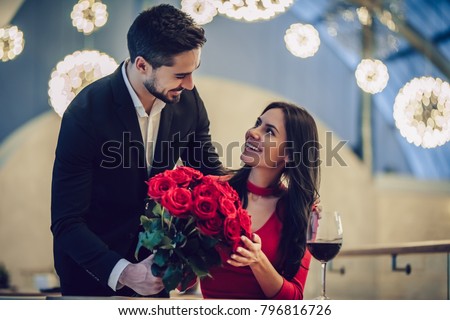 Beautiful loving couple is spending time together in modern restaurant. Attractive young woman in dress and handsome man in suit are having romantic dinner. Celebrating Saint Valentine's Day. Royalty-Free Stock Photo #796816726