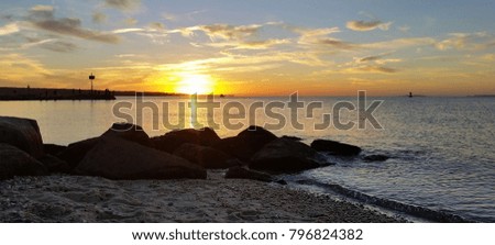 Summer Ocean Sunrise/Sunset of Bright Yellows and Oranges, Just Peeking Over the Horizon, with Dark Rocks and Sand Textures in the Foreground