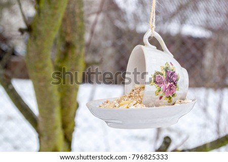 Teacup bird feeder made from a vintage cup and saucer glued together. Teacup bird feeder hanging on a tree. Royalty-Free Stock Photo #796825333