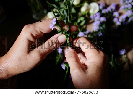 Close up on hands of woman working on a bouquet of flowers in a vase.Florist woman decorate White roses and Purple Marguerite Daisy flowers on wooden table.People and floral arrangement concept.