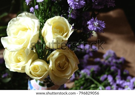 Florist woman decorate White roses and Purple Marguerite Daisy flowers in a vase on wooden table in natural light.People and floral arrangement concept.