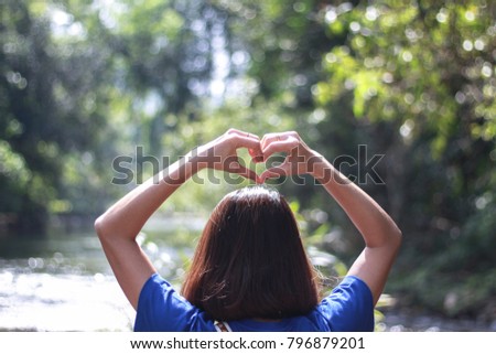 The girl made heart shaped hands on nature green bokeh sun light and blurred leaf abstract background , Valentine's Day