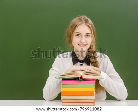 Happy teen girl with books on the background of a school board