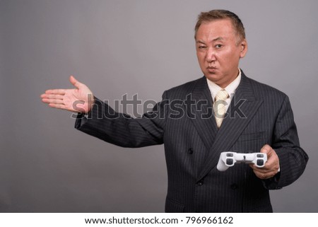 Studio shot of mature Asian businessman playing games against gray background