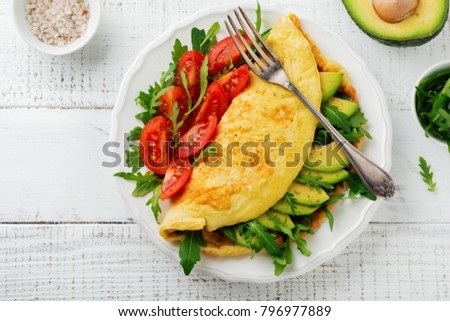 Omelette with avocado, tomatoes and arugula on white ceramic plate on light stone background. Healthy breakfast. Selective focus. Top view. Copy space. Royalty-Free Stock Photo #796977889