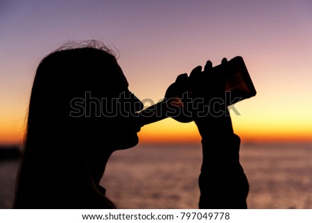 silhouette of a girl drinking alcohol from a bottle at sunset
