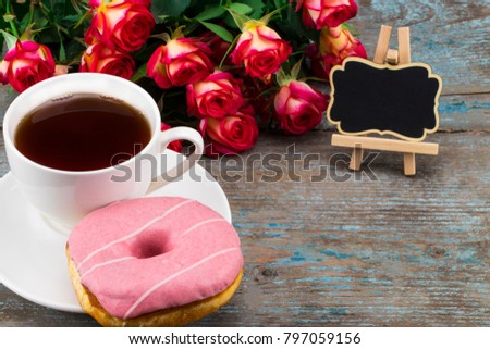 Cup of tea with donut, fresh roses and blackboard with space for your text  on a wooden background. Perfect image for mother's day.