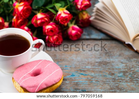 Cup of tea with donut, fresh roses and book  on a wooden background. Perfect image for mother's day.