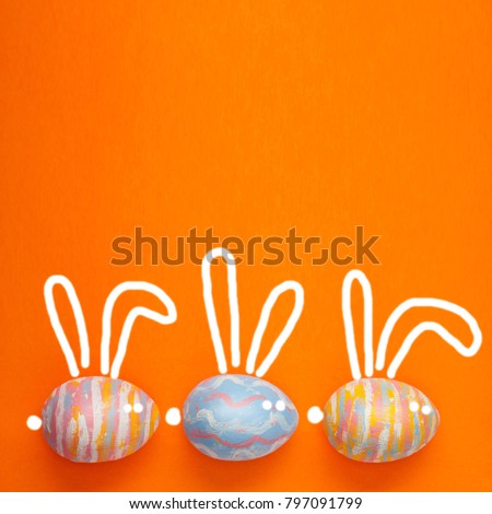 Easter colored eggs on a orangebackground, with painted hare ears. Background for a postcard, Easter concept, space for text