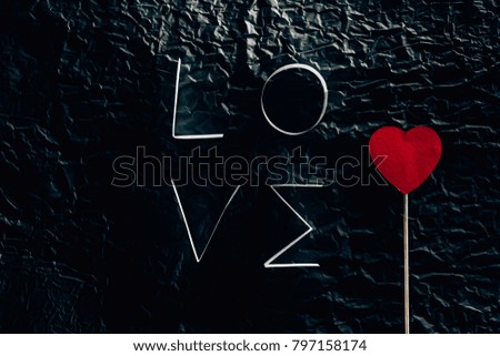 word LOVE made of paper stripes with heart on stick on black concrete surface