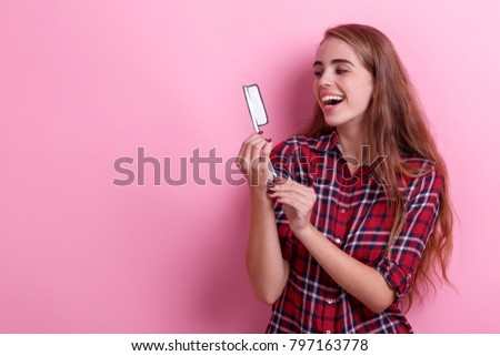 A cheerful girl, holds a paper toothbrush, looks at it and laughs. Hygiene concept. On a pink background.