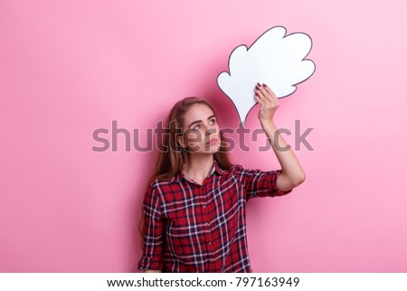 A pensive girl, holds a paper image of thought or idea overhead and looks up. On a pink background.