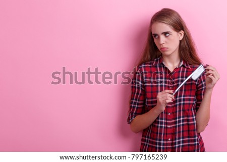 A gloomy girl , holds a paper toothbrush and looks away. Hygiene concept. On a pink background.