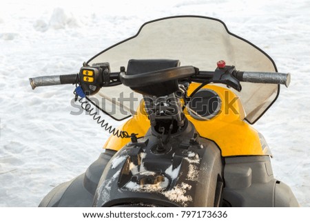 A yellow snowmobile stands in the snow near the hut.