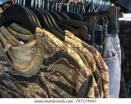 Set of many multi-coloured clothes ,jacket with camouflage pattern ,blue jeans on hanging In the store
