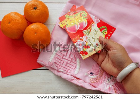 Woman's hand hold red packet(Ang pow) on white wooden background top view for copy space,concept for Chinese new year festival,English translation for the foreign text means blessing and happiness