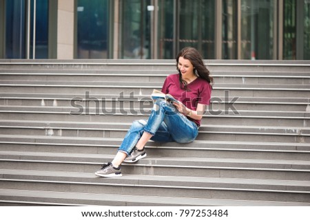 Beautiful woman reading a book on the steps of the building. 
