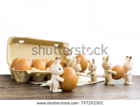 Rabbit dolls are preparing to celebrate Easter.Rabbits are lifting eggs from paper crates to use in Easter on a white background on a wooden table.