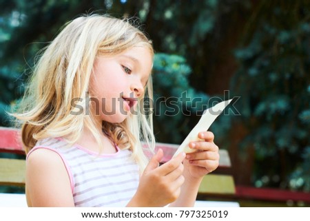 Beautiful Caucasian blond girl sitting on old park bench drawing picture