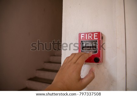 The hand is pulling fire alarm signal on the wall next to the door 